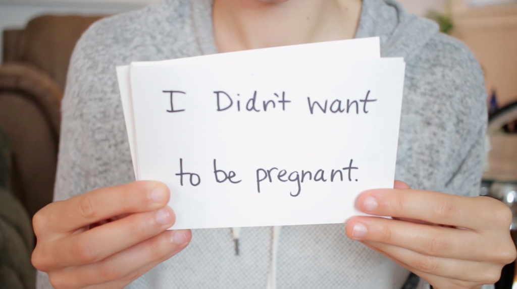 girl with card that says 'I didn't want to be pregnant'