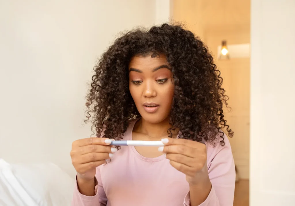 young surprised woman looks at positive pregnancy test and believes unplanned pregnancy myths